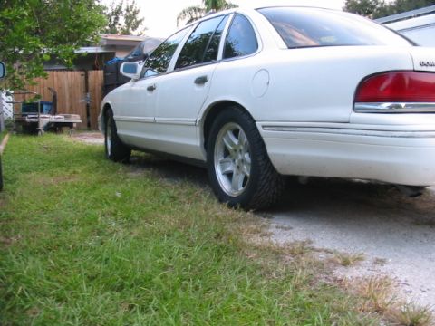 1997 Ford Crown Victoria - The rear side profile of a white 1997 Ford Crown Victoria sedan is visible, parked outdoors.