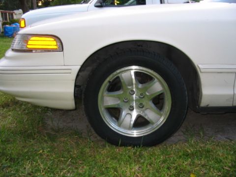 1997 Ford Crown Victoria - Front fender and wheel of a white 1997 Ford Crown Victoria, parked next to another vehicle.