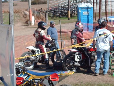 1995 Ford Probe - Racers and their motorcycles are gathered at a dirt track event, with spectators and facilities visible.
