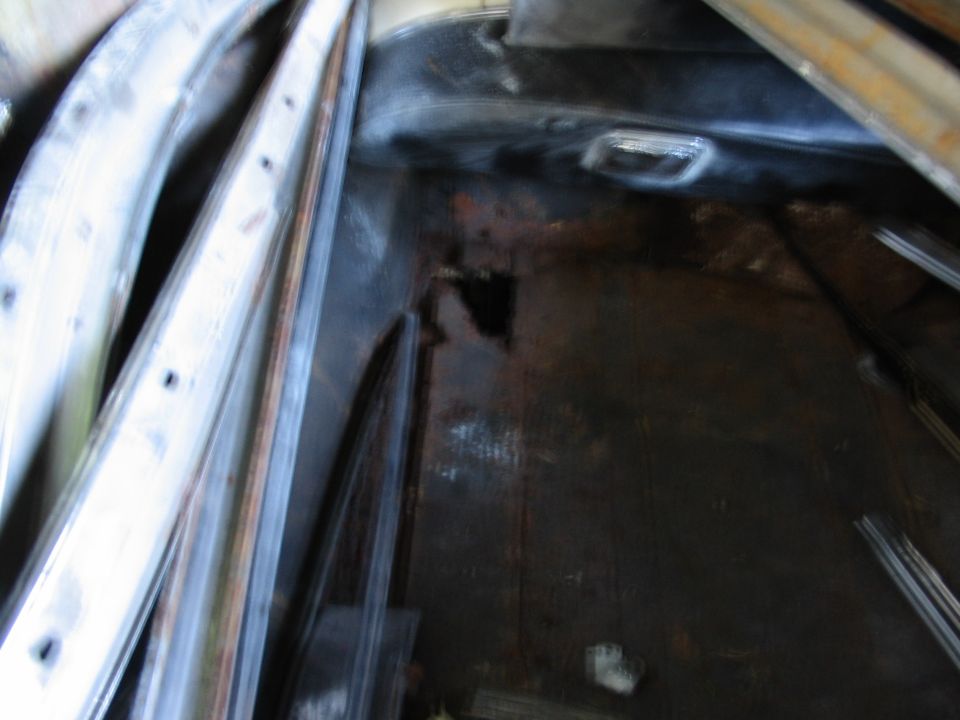 Rusted-through trunk floor pan with hole, chrome trim pieces stacked nearby
