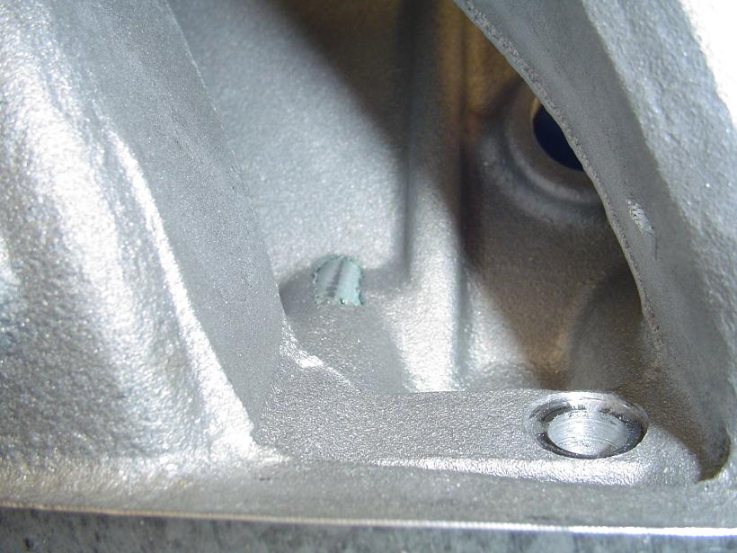 Close-up of a cast metal engine component with a small blue mark and a threaded hole