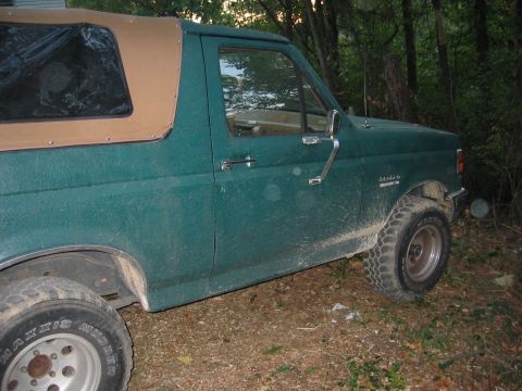 1990 Ford Bronco - This green Ford Bronco, seen from the side, has a tan soft top and appears to be from the late 1980s.