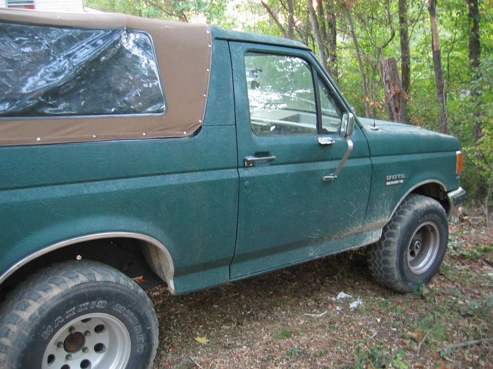 Green 1990 Ford Bronco with brown soft top, side view