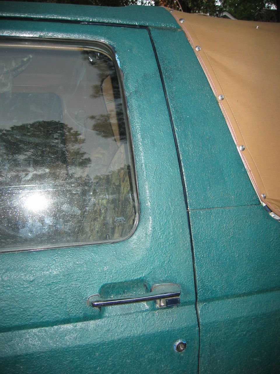 Green Ford Bronco door handle and side panel with a tan soft top