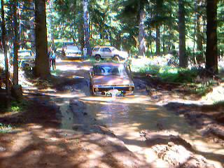 1976 Ford F-100 - A vintage Ford pickup truck navigates a muddy path in a forest, with other vehicles visible in the background.