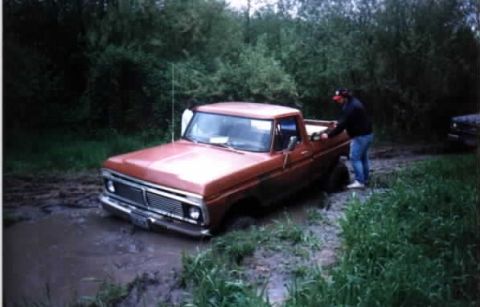1976 Ford F-100 - Orange 1976 Ford F-100 stuck in a muddy area with a person nearby.