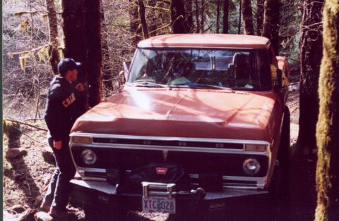 1976 Ford F-100 - A person stands by a red pickup truck in a wooded area. The license plate reads XTC 028.