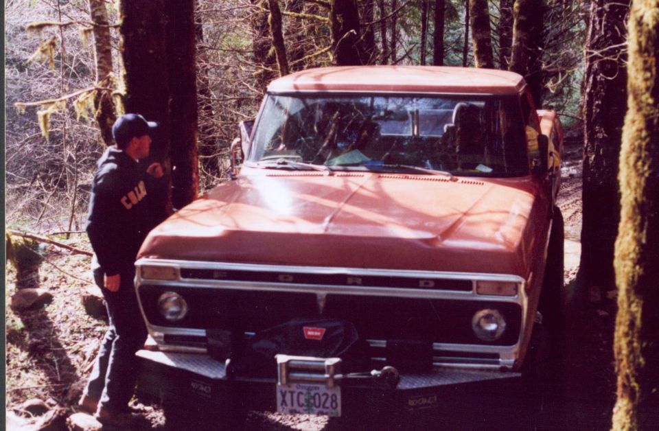 Red 1970s Ford pickup with covered Warn winch parked among mossy forest trees