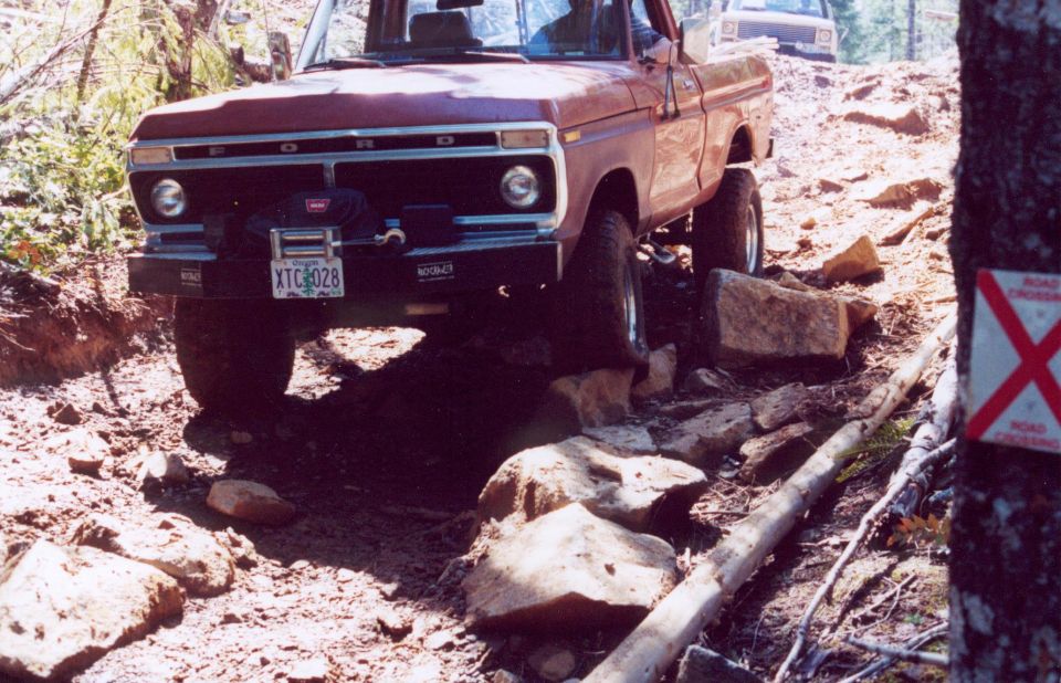 Red 1970s Ford 4x4 pickup with Warn winch crawling over rocks on a trail