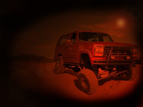 1984 Ford Bronco - This lifted 1980s Ford Bronco, equipped with a bull bar and large off-road tires, is captured in a desert setting under a dramatic sky.