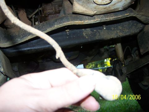 1979 Ford F-150 - Close-up view of a vehicle's undercarriage, with a hand obscuring part of the frame and a wire.