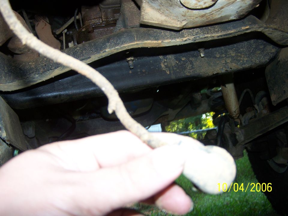 Undercarriage of a vehicle, showing frame and suspension components. A hand holds a wire in the foreground. Date stamp reads 10/04/2006
