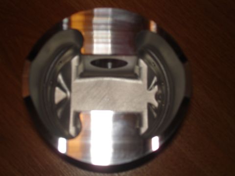 1994 Ford Probe - A close-up view of a metal piston, showing its internal machining and circular outer edge, resting on a wood-grain background.
