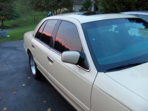 1996 Mercury Grand Marquis - A tan sedan is parked on a driveway with a sunset reflected in its windows.