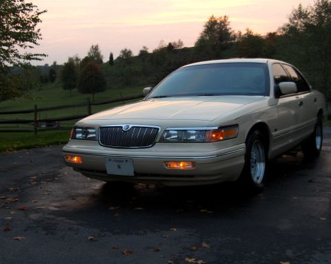 1996 Mercury Grand Marquis - A 1996 Mercury Grand Marquis is parked on a wet driveway with fallen leaves during sunset.