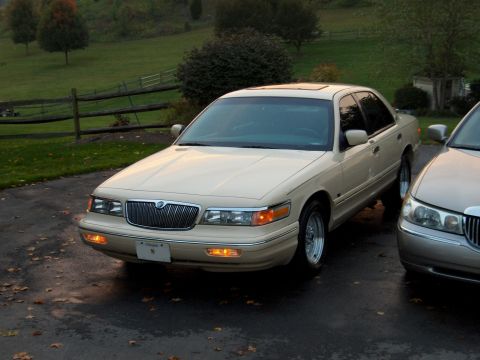 1996 Mercury Grand Marquis - A 1996 Mercury Grand Marquis is parked on a wet driveway with fallen leaves scattered around.