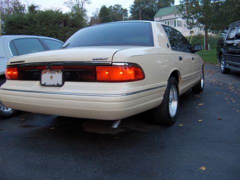 1996 Mercury Grand Marquis - The rear of a tan Mercury Grand Marquis is visible, parked on an asphalt surface with fallen leaves.
