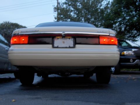 1996 Mercury Grand Marquis - Rear view of a beige sedan, possibly a 1995 Mercury Grand Marquis, with its brake lights on.