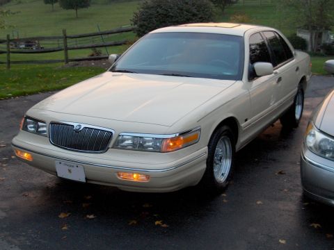 1996 Mercury Grand Marquis - A cream-colored Mercury Grand Marquis is parked on a wet driveway next to another vehicle.