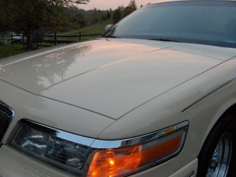 1996 Mercury Grand Marquis - A cream-colored sedan's front end is visible in this close-up shot, with a hint of the surrounding landscape.