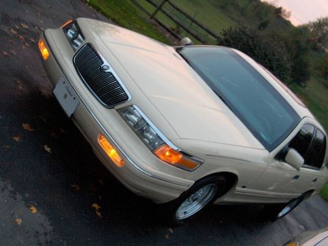 1996 Mercury Grand Marquis - A cream-colored 1996 Mercury Grand Marquis is parked on a wet asphalt surface with scattered autumn leaves.