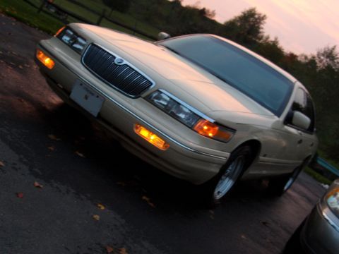 1996 Mercury Grand Marquis - A tan Mercury Grand Marquis is parked on a wet road with fallen leaves, as dusk settles.