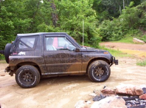 1996 Chevrolet Tracker - A muddy 1996 Chevrolet Tracker 4x4 is parked on a dirt path surrounded by trees.