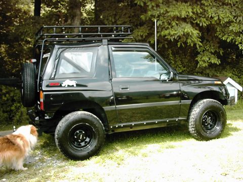 1996 Chevrolet Tracker - A black 1996 Chevrolet Tracker is parked on a grassy area with a dog nearby.