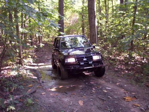 1996 Chevrolet Tracker - Black 1996 Chevrolet Tracker navigates a wet, muddy trail in a forest.