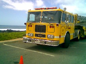 1991 Ford Bronco - A yellow fire truck is parked in a lot with the ocean in the background.