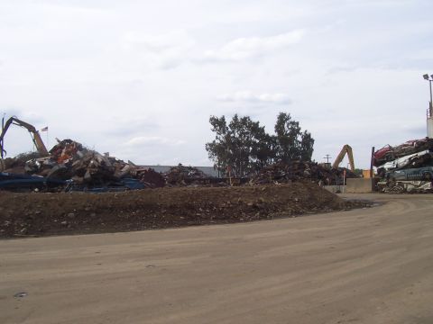 1994 Ford F-150 - Scrap metal yard with heavy machinery and stacked vehicles under a cloudy sky.