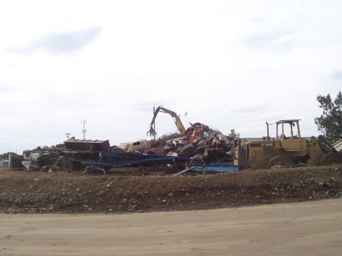 1994 Ford F-150 - A junkyard scene a large pile of scrap metal and heavy machinery under a cloudy sky.