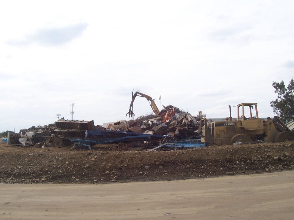 Junkyard scene with a pile of scrap metal, a claw crane, and a yellow front-end loader