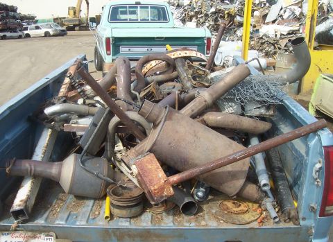1994 Ford F-150 - A light blue pickup truck, likely from the 1970s, carries a load of scrap exhaust system parts in its bed.