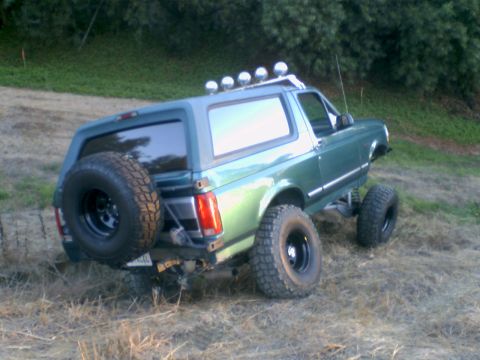 1996 Ford Bronco - This lifted green SUV, possibly a 1996 Ford Bronco, is shown from a 3/4 rear angle on a grassy incline.