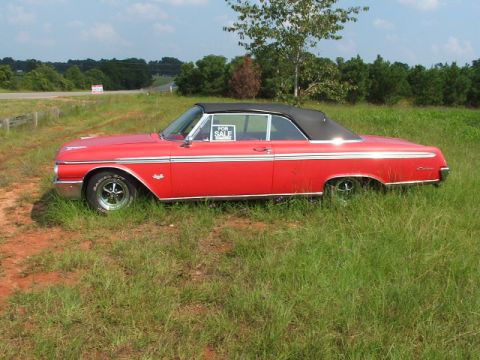 1966 Ford Ranchero - A red 1966 Ford Ranchero convertible with a black top is parked in a grassy field, displaying a 'For Sale' sign.