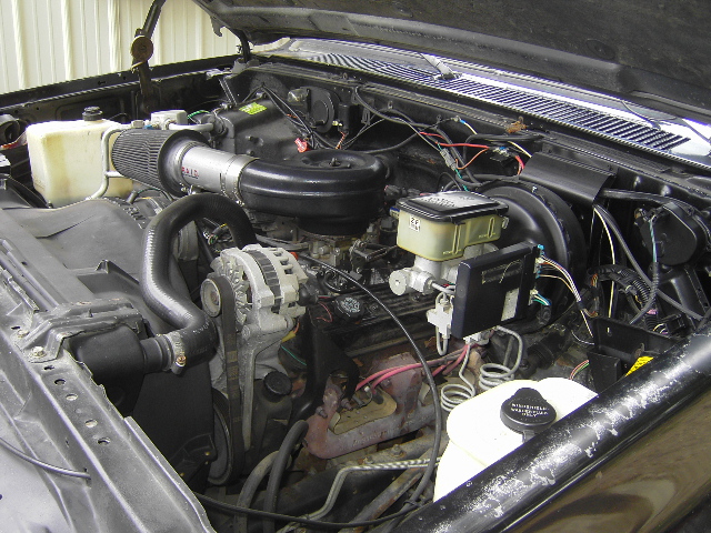 Engine bay of a 1990 Chevrolet Suburban, showing the V8 engine, alternator, air intake, and brake fluid reservoir