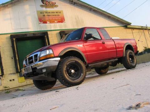 1974 Ford F-100 - A red pickup truck is parked on a dirt road in front of a building with a sign.