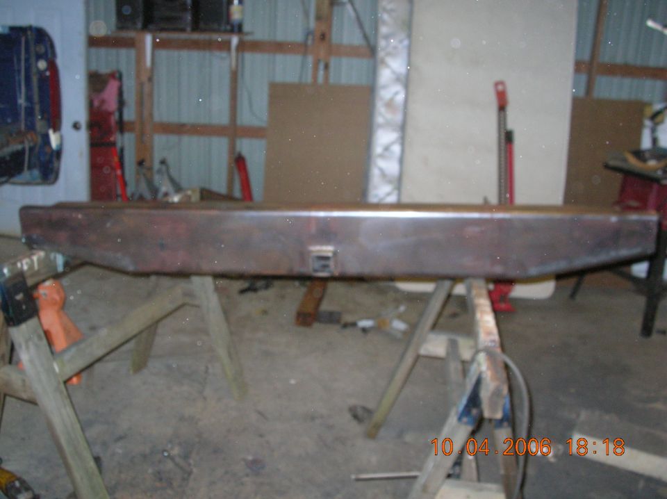 Rusty metal rear bumper with a hitch receiver opening, resting on sawhorses
