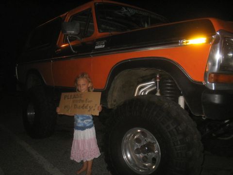 1979 Ford Bronco - A young girl stands in front of a lifted orange Ford Bronco, holding a cardboard sign.