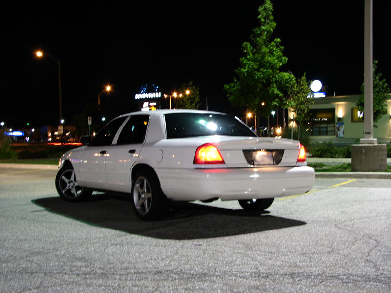 White full-size sedan at night in a parking lot, rear three-quarter view with tail lights lit