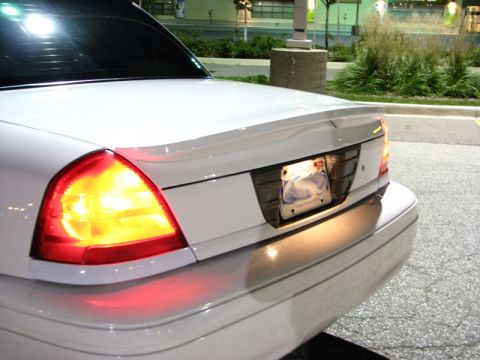 2003 Ford Crown Victoria - Night shot of the driver-side rear corner of a white Ford Crown Victoria, with the amber turn signal lit inside the clear-and-red taillight…