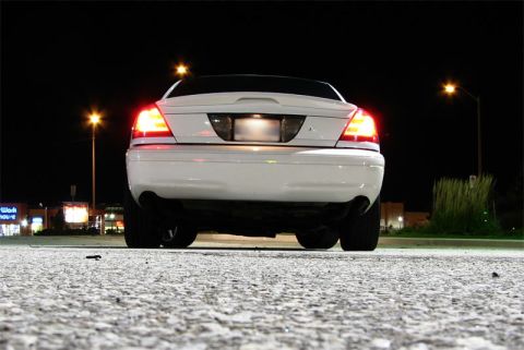 2003 Ford Crown Victoria - Low ground-level rear shot of a white Ford Crown Victoria at night in a parking lot, tail lights and license-plate lamps lit and trunk lid…