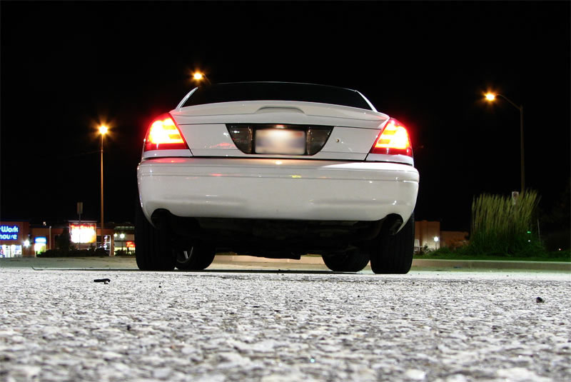 Ground-level rear view of white Crown Victoria at night with tail lights lit