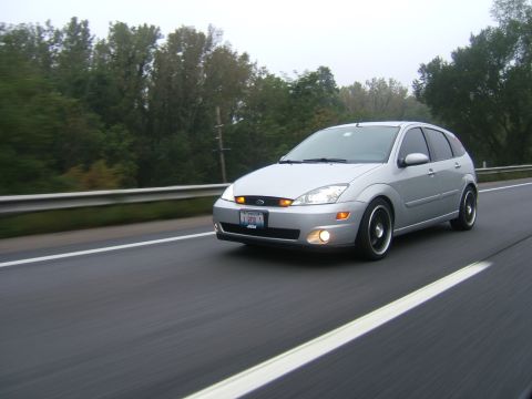 2003 Ford Focus - A silver 2003 Ford Focus hatchback is seen driving on a highway under an overcast sky.