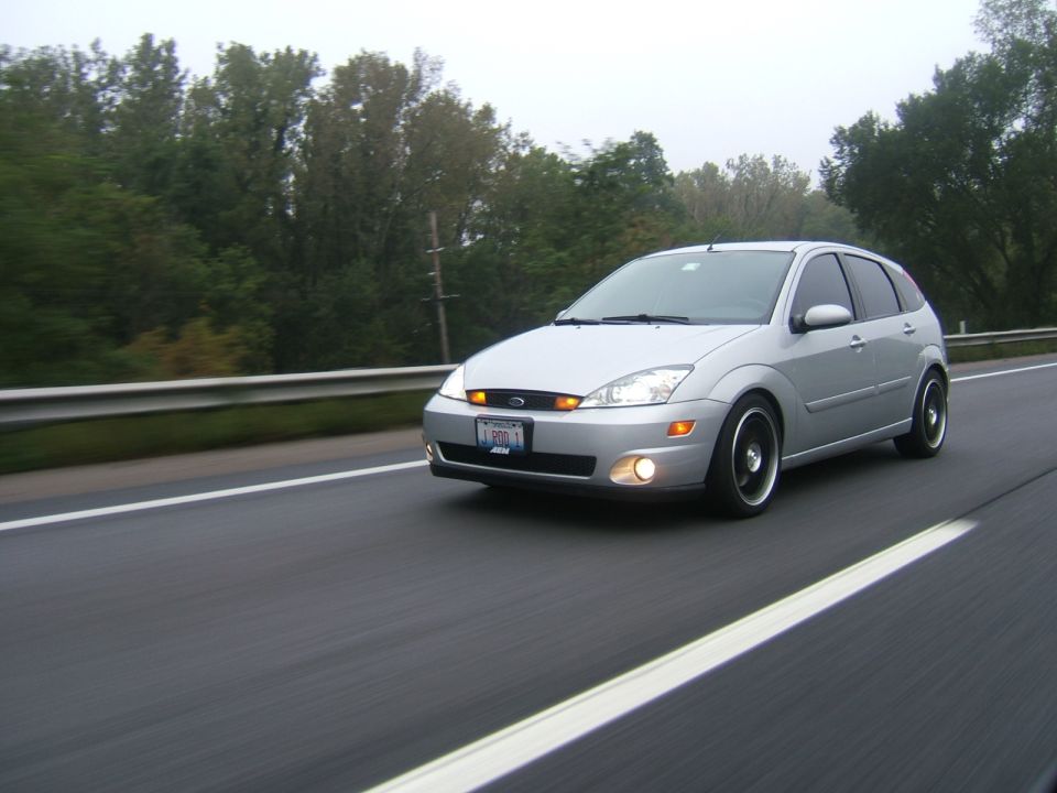 Silver Ford Focus hatchback driving on a highway with fog lamps on, motion blur
