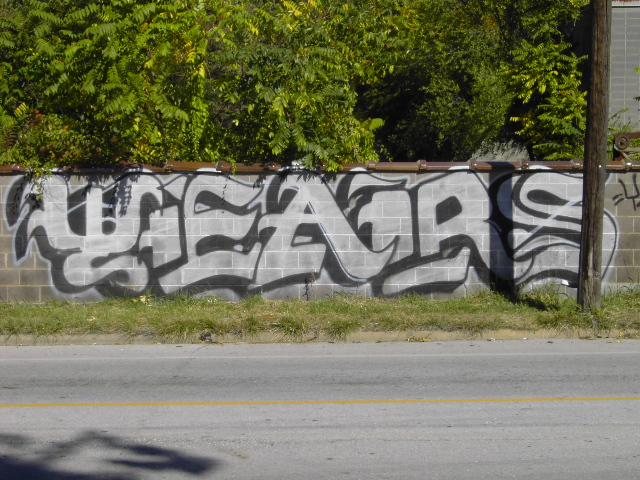 Silver and black graffiti on a concrete block wall beside a roadway