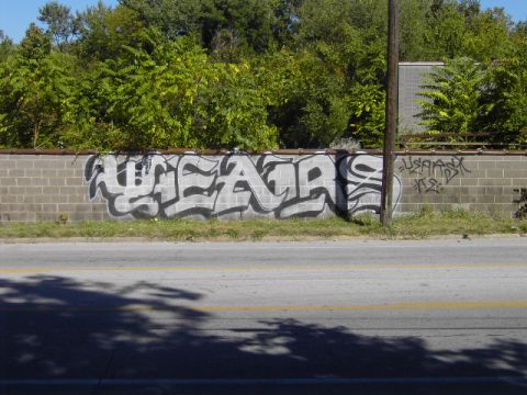 1991 Ford Bronco - Graffiti covers a cinder block wall along a road, with trees in the background and a utility pole to the right.