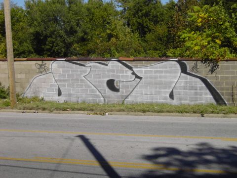 1991 Ford Bronco - Graffiti art adorns a cinder block wall beside a road with trees in the background.