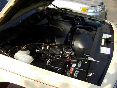 1996 Mercury Grand Marquis - Engine bay of a white vehicle with the hood open, showing a black engine cover with a gold emblem, black air intake ducting, coolant reserv…